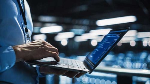 man standing up holding a laptop while typing with the other hand